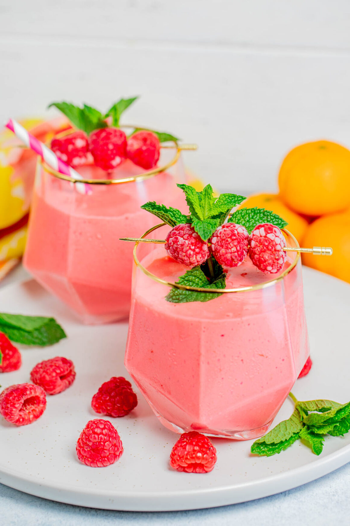 2 short glasses with raspberry smoothie recipes with a skewer of fresh raspberries for garnish