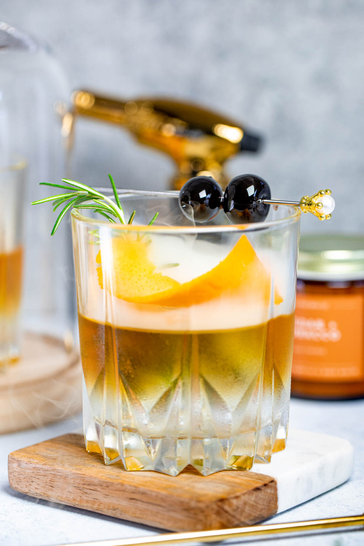 smoked whiskey serve into a short glass with smoke and marashinos cherries, rosemary sprig and orange twist for garnish