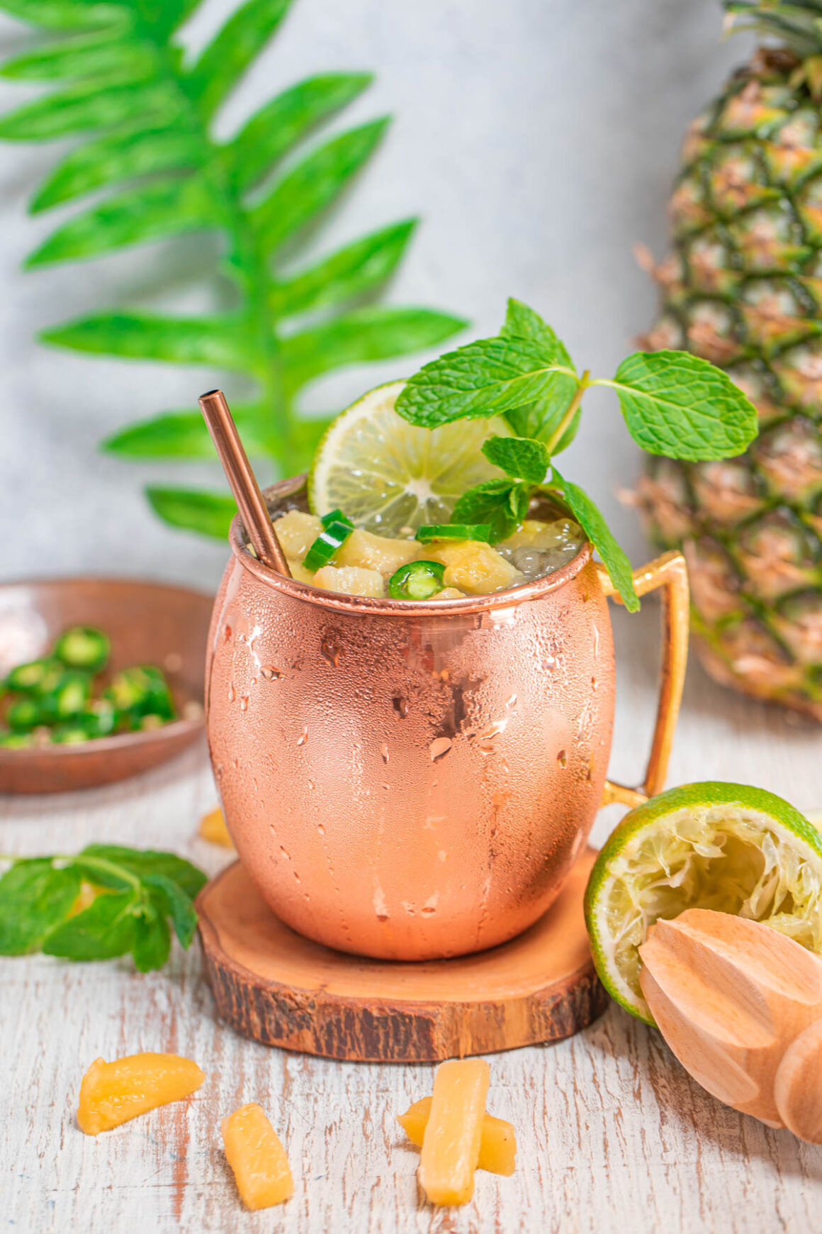 1 pineapple spicy moscow mule in a copper mug with a few jalapeños and pineapple chunks like a garnish