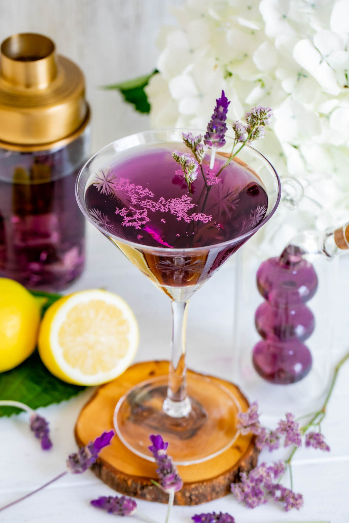 lavender martini served in a martini glass with white flowers on the background