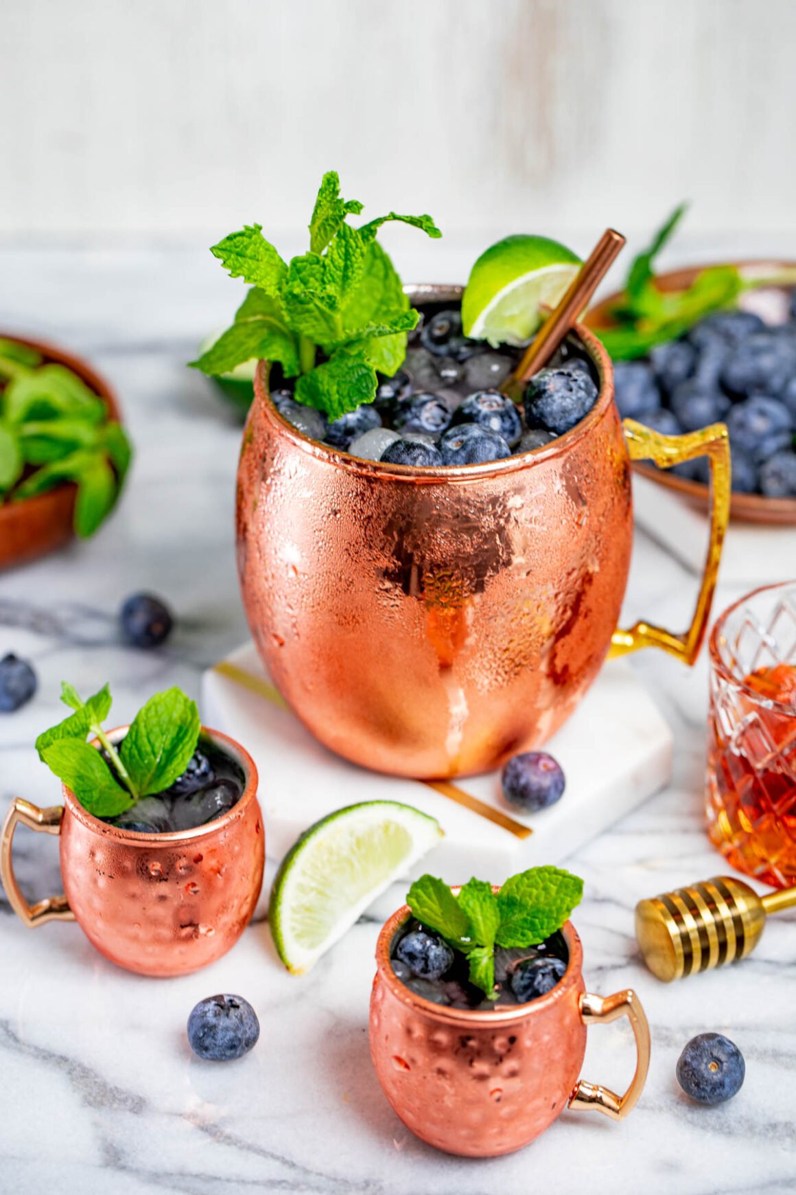 1 copper mug and 2 tiny ones with blueberries moscow mule cocktails 